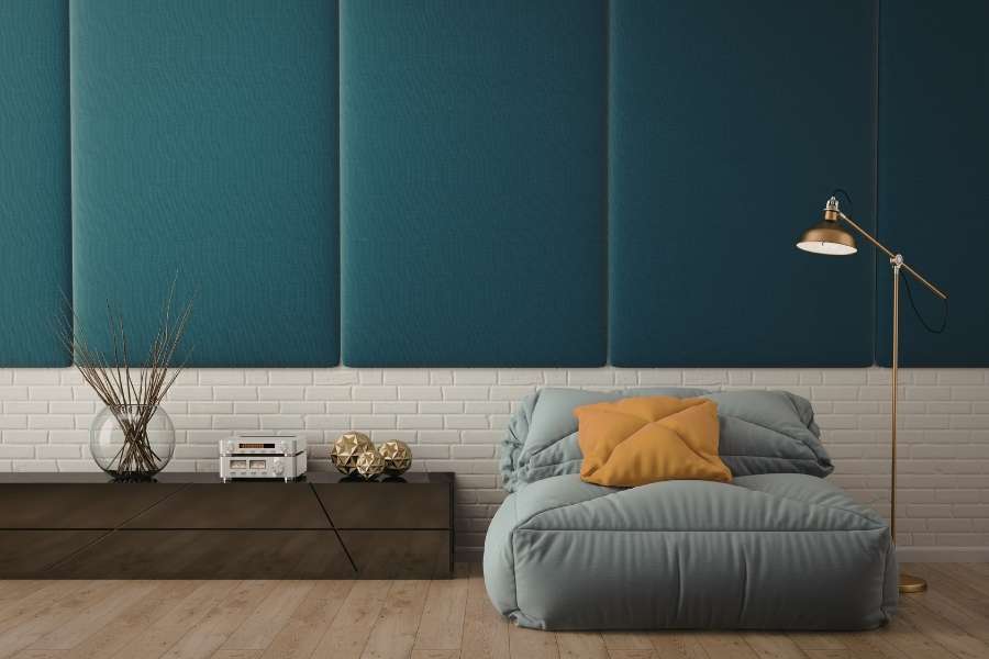 An accent wall in a modern living room featuring large, vertical, upholstered teal fabric panels above a white painted brick base.