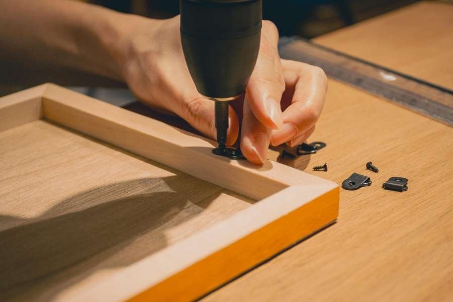 Close-up of hands using a power screwdriver to attach hardware to a small wooden frame, illustrating smart scrap wood projects.