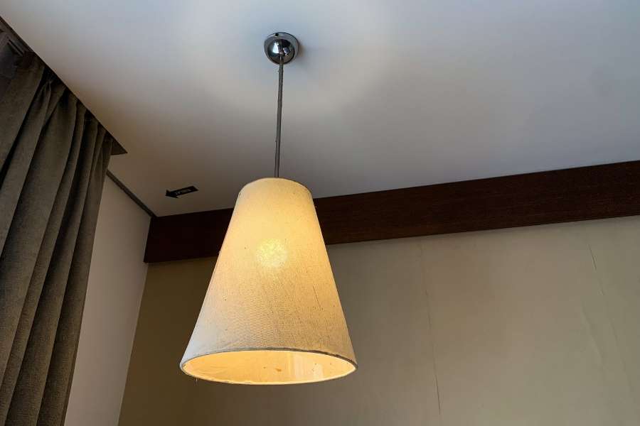 A conical fabric pendant light placement hanging near a plain interior wall and curtains.